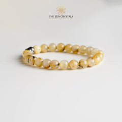 golden rutile bracelet with a silver clasp on a light gray background, branded 'The Zen Crystals'.