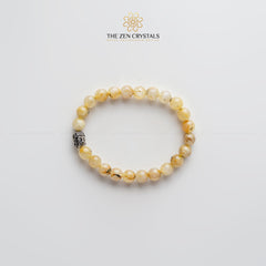golden rutile bracelet with a silver charm on a light gray background, branded 'The Zen Crystals'.