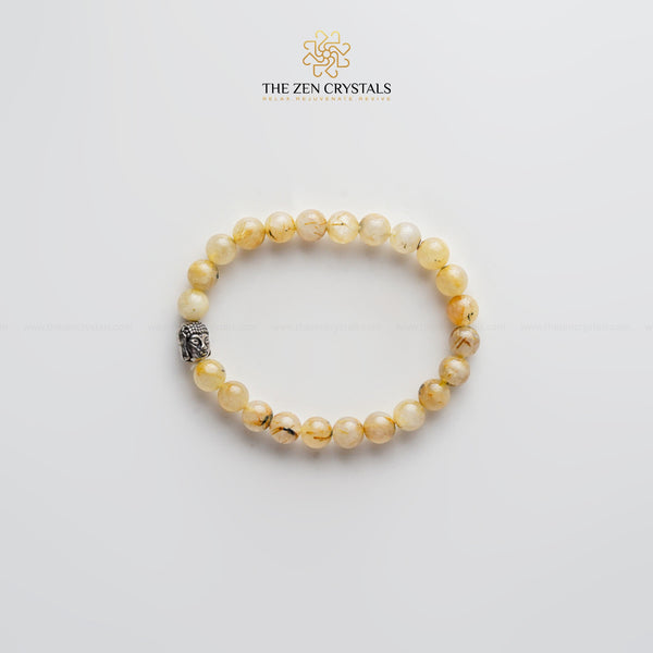 golden rutile bracelet with a silver charm on a light gray background, branded 'The Zen Crystals'.