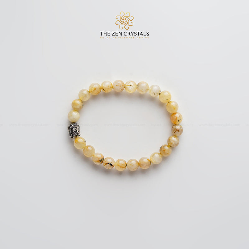 golden rutile bracelet with a silver charm on a light gray background, branded 'The Zen Crystals'.