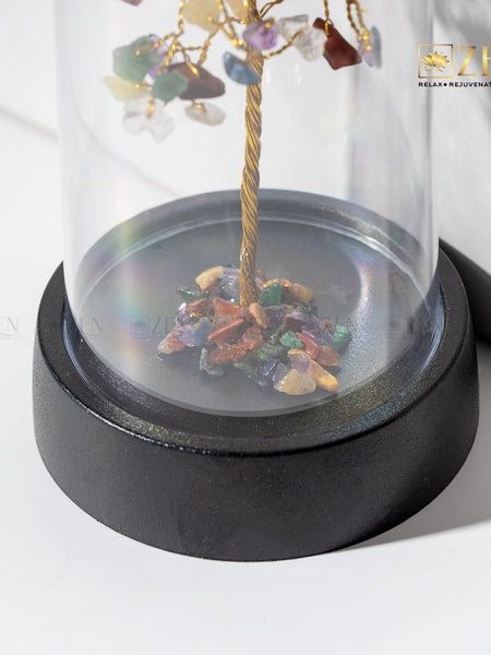 Decorative item with multicolored stones and a gold branch inside a glass dome on a white background.