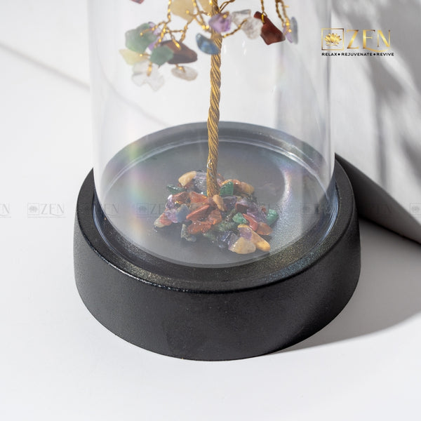Decorative item with multicolored stones and a gold branch inside a glass dome on a white background.