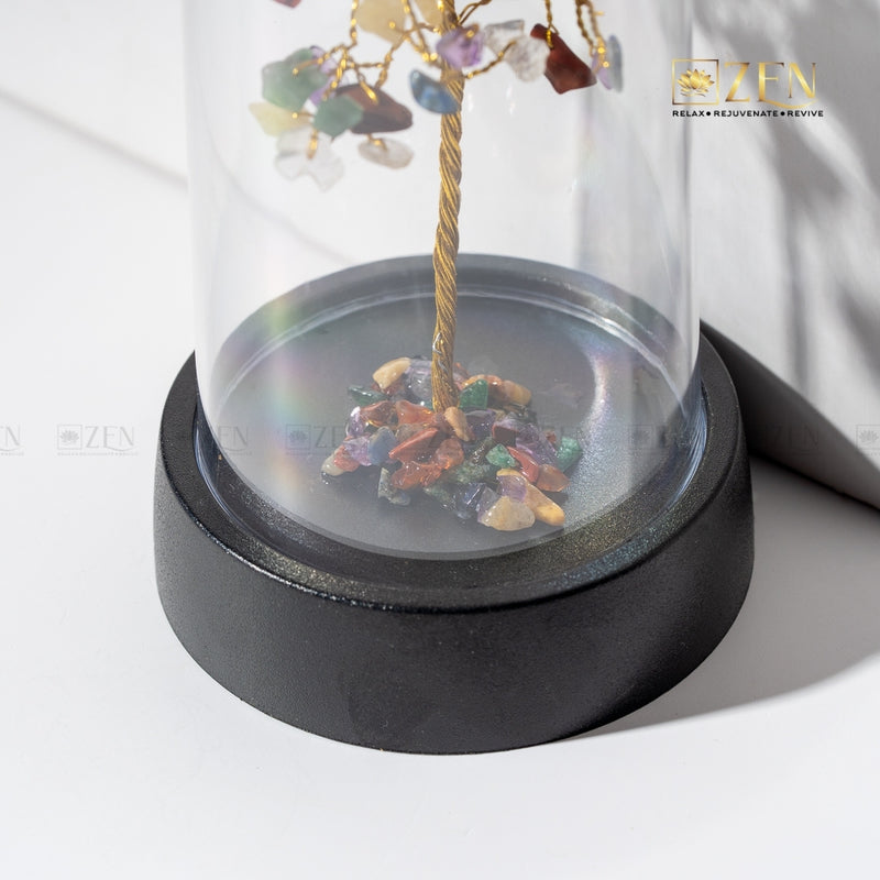 Decorative item with multicolored stones and a gold branch inside a glass dome on a white background.
