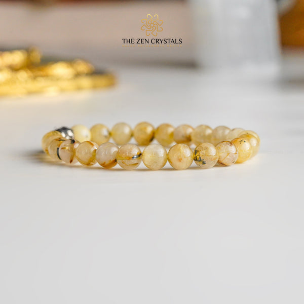 golden rutile bracelet on a white surface with 'The Zen Crystals' branding.