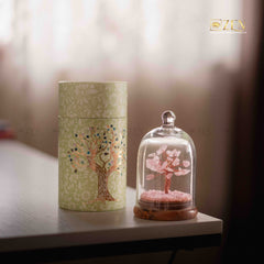 Decorative tree inside a glass dome and cylindrical container with tree design on a blurred background