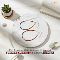 Red Jasper anklets on a marble surface with a plant and book in the background, featuring the brand 'ZEN'.