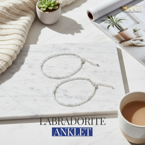 Labradorite anklet on a marble surface with a cup of tea, plant, and blanket.