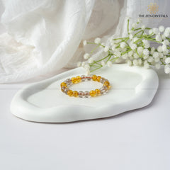 Success & Protection Energy Bracelet on a white stone with white flowers and 'The Zen Crystals' branding.