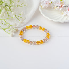 Success & Protection Energy Bracelet with yellow and clear beads on a white surface with flowers.