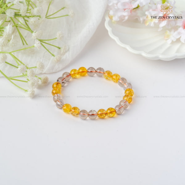 Success & Protection Energy Bracelet with yellow and clear beads on a white surface with flowers.