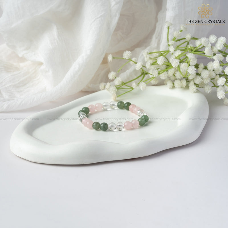 Harmony In Relationship Bracelet with green and pink beads on a white dish with white flowers, branded 'The Zen Crystals'.