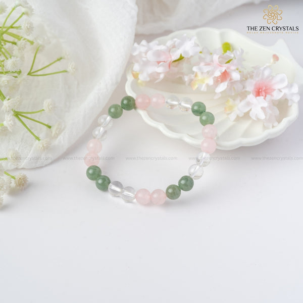 Harmony In Relationship Bracelet with green, pink, and clear beads on a white surface with flowers and a shell.
