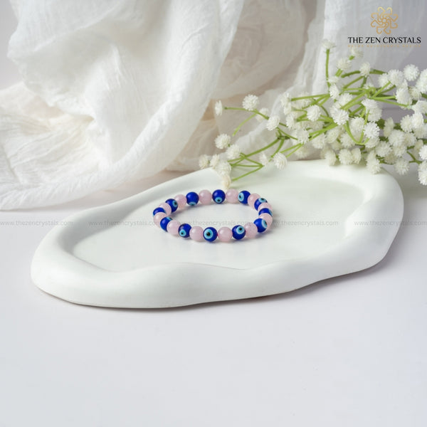Love & Protection Energy Bracelet with blue and pink beads on a white dish with white flowers and white fabric in the background, branded 'The Zen Crystals'.