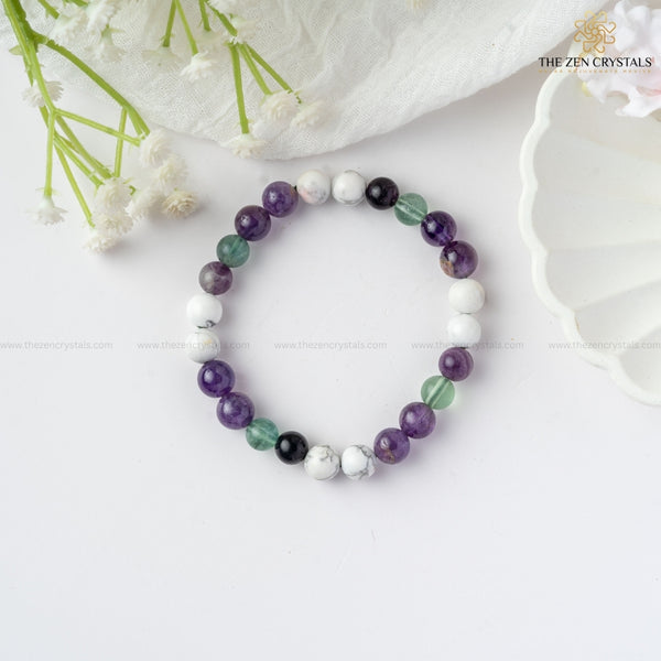 clarity of thoughts bracelet with purple, green, and white beads on a white surface with flowers and a shell in the background.