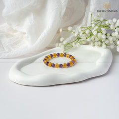 Success Alignment Energy Bracelet on a white dish with white flowers and a white fabric background, branded 'The Zen Crystals'.