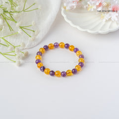 Success Alignment Energy Bracelet with purple and yellow beads on a white surface with flowers.