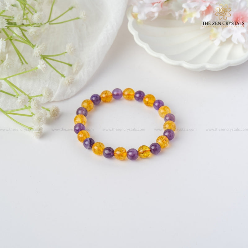 Success Alignment Energy Bracelet with purple and yellow beads on a white surface with flowers.