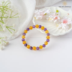 Success Alignment Energy Bracelet with purple and orange beads on a white surface with flowers and shells.