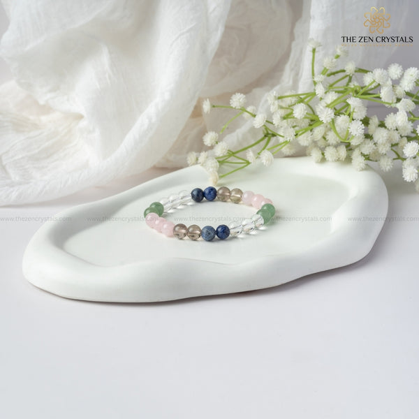 Inner Peace Energy Bracelet on a white dish with white flowers and soft fabric background, branded 'The Zen Crystals'.