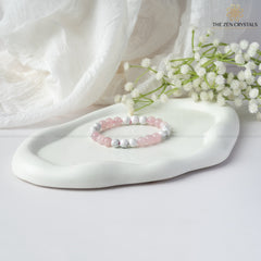 Love Energy Bracelet on a white dish with white flowers and soft fabric background, brand 'The Zen Crystals' visible.