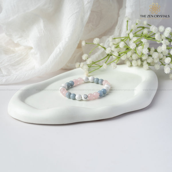 peaceful meditation bracelet with pastel beads on a white dish with white flowers, branded 'The Zen Crystals'.