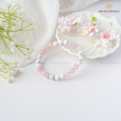 Love Energy Bracelet with pink and white beads on a white surface with flowers and a shell.