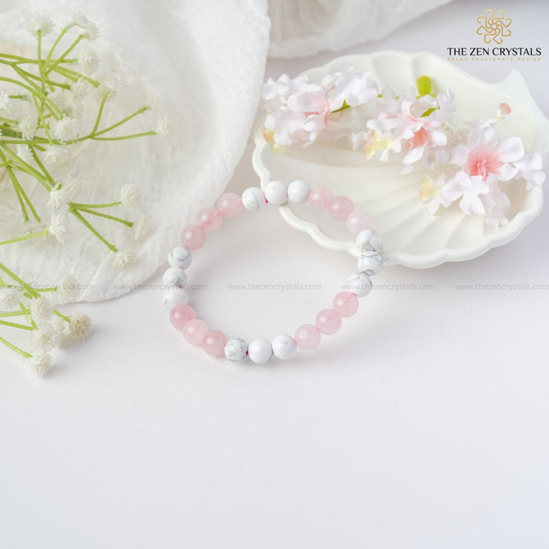 Love Energy Bracelet with pink and white beads on a white surface with flowers and a shell.
