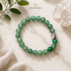 Green aventurine bracelet with Buddha charm on a marble surface, branded 'The Zen Crystals'.