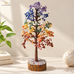 7 chakra 1000 chips crystal tree of life sculpture on a round wood slice base, styled on a beige tabletop with a plant and stone in the background.