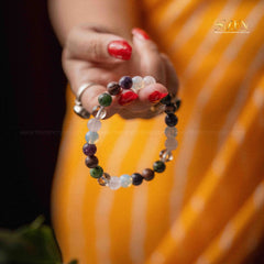 Close-up of a hand wearing a colorful beaded bracelet with a blurred orange background