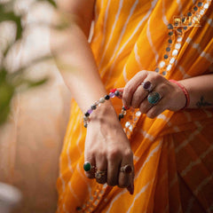 Person wearing an orange saree with jewelry, including rings and a ruling number 7 bracelet.