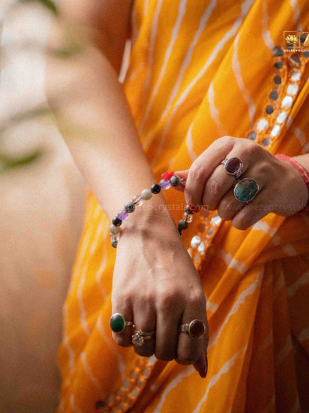 Person wearing an orange saree with jewelry, including rings and a ruling number 7 bracelet.