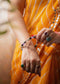 Person wearing an orange saree with jewelry, including rings and a ruling number 7 bracelet.