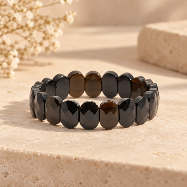 Faceted Black Obsidian bracelet arranged in a circle on a light beige stone surface with dried flowers in the background.