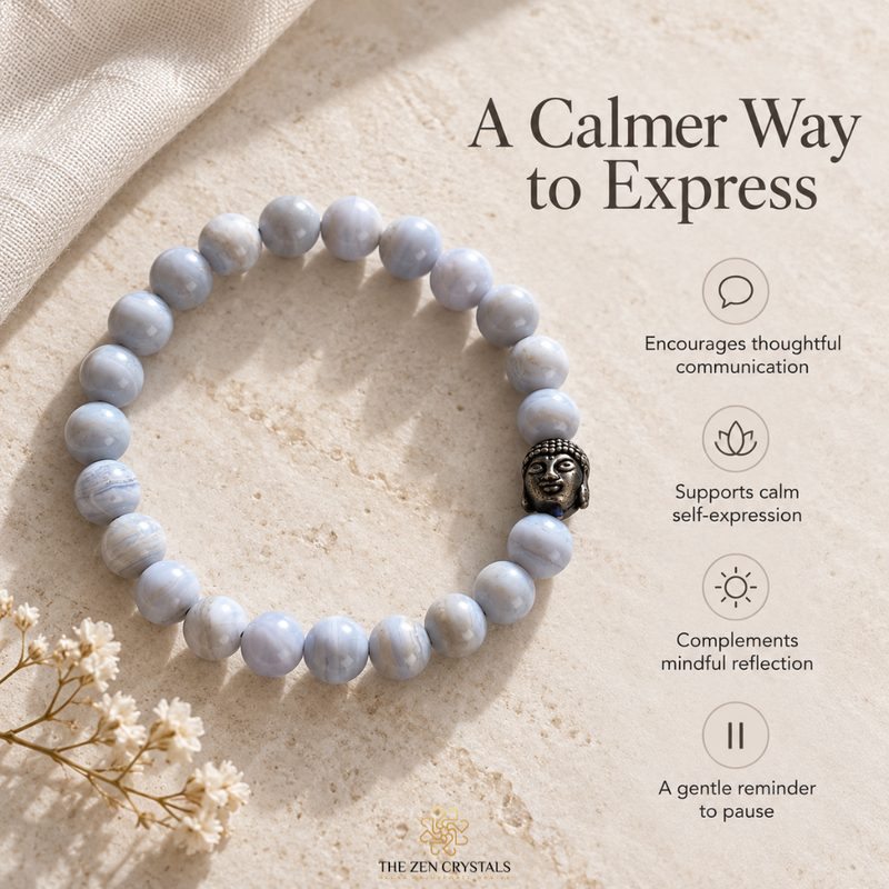 A beaded stretch bracelet made of pale blue-gray marbled round beads with a small dark metal Buddha charm, displayed on a textured beige stone surface with decorative fabric and dried flowers. Text on the right reads 'A Calmer Way to Express' with feature callouts, and 'THE ZEN CRYSTALS' appears at the bottom.