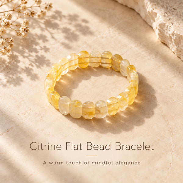 A citrine flat bead bracelet made of translucent yellow gemstone beads, displayed on a textured beige stone surface with soft shadows and dried flowers in the corner. Text below reads 'Citrine Flat Bead Bracelet' and 'A warm touch of mindful elegance'.