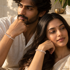 A man and a woman wearing matching clear crystal bracelets, posed closely together in a warm, sunlit setting.
