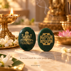 Two dark green polished stone pooja flags with gold foil designs, one depicting a seated deity and the other a Shiva triangle, displayed on a marble surface with a burning brass diya, white flowers, and incense in a serene, spiritual setting.