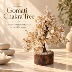 The Zen Crystals Gomati Chakra Tree, a decorative statement piece made of white and beige gemstone petals on a dark brown wire frame and rustic brown cylindrical base, displayed on a stone surface with stacked stones and a vase in the background.