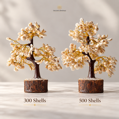 Two decorative miniature flowering trees made from shell beads and gold wire, displayed side by side on a light surface with a soft neutral background. Text below reads '300 Shells' and '500 Shells', and the brand name 'THE ZIN CRYSTALS' appears at the top.
