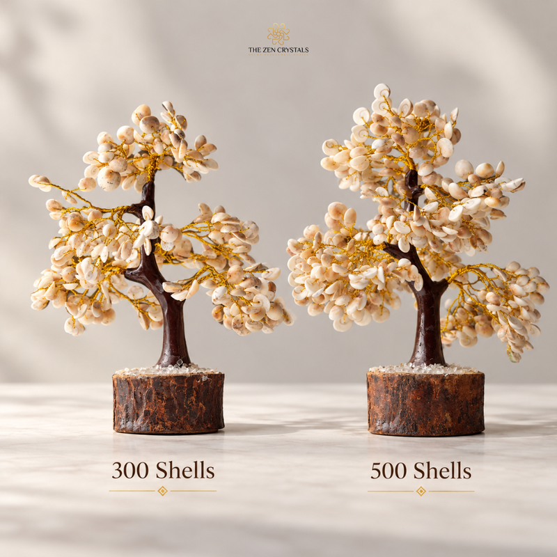 Two decorative miniature flowering trees made from shell beads and gold wire, displayed side by side on a light surface with a soft neutral background. Text below reads '300 Shells' and '500 Shells', and the brand name 'THE ZIN CRYSTALS' appears at the top.