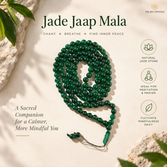 A coiled green jade bead mala necklace with a tassel and cord lies on a light beige textured surface with decorative leaves and stones around it. Text reads 'Jade Jaap Mala' with smaller copy 'Chant + Breathe + Find Inner Peace,' and icons note natural jade stone, meditation and prayer support, and daily mindfulness.