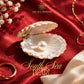 south sea pearl on red fabric, surrounded by gold jewelry and white flowers, with 'The Zen Crystals' branding.