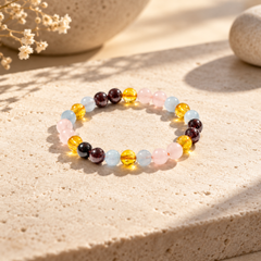A beaded stretch bracelet with translucent round beads in pink, light blue, yellow, and dark brown, displayed on a textured beige stone surface with soft natural shadows.