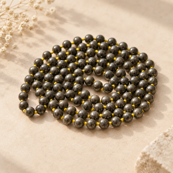 Pyrite Jaap mala displayed on a textured beige surface with dried flowers in the corner.
