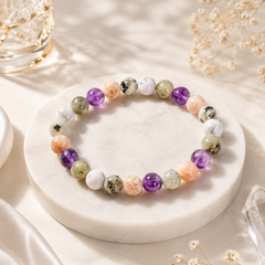RULING NUMBER 2 BRACELET made of polished multicolored gemstone beads, displayed on a round white marble stand with dried flowers and soft sunlight.