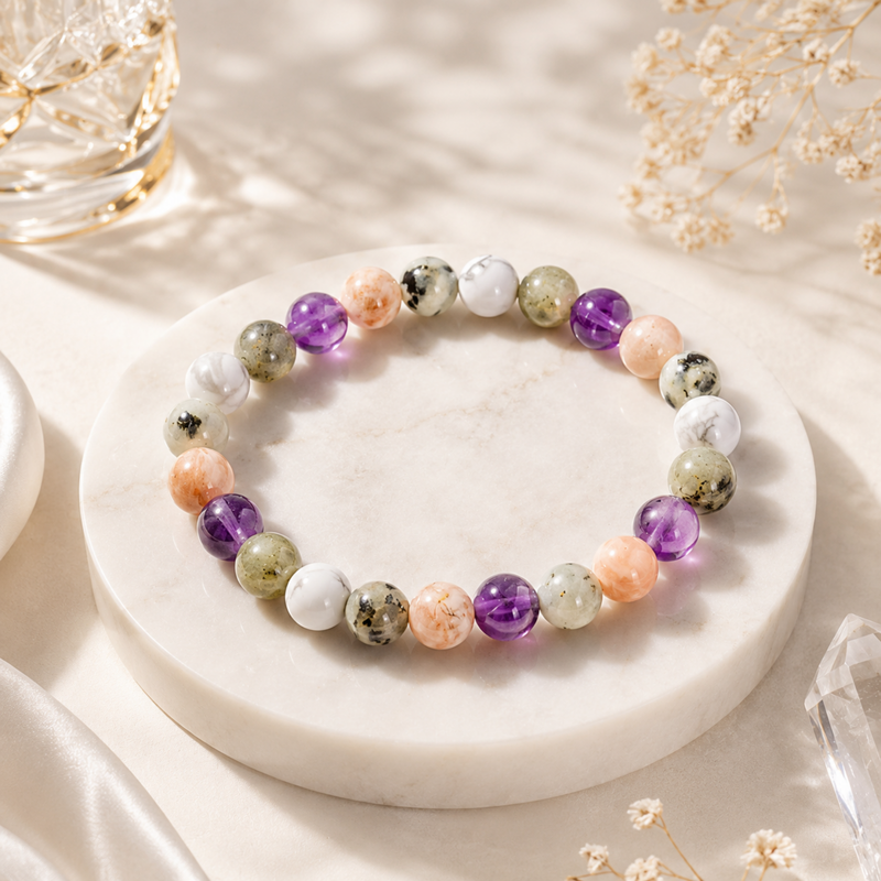 RULING NUMBER 2 BRACELET made of polished multicolored gemstone beads, displayed on a round white marble stand with dried flowers and soft sunlight.