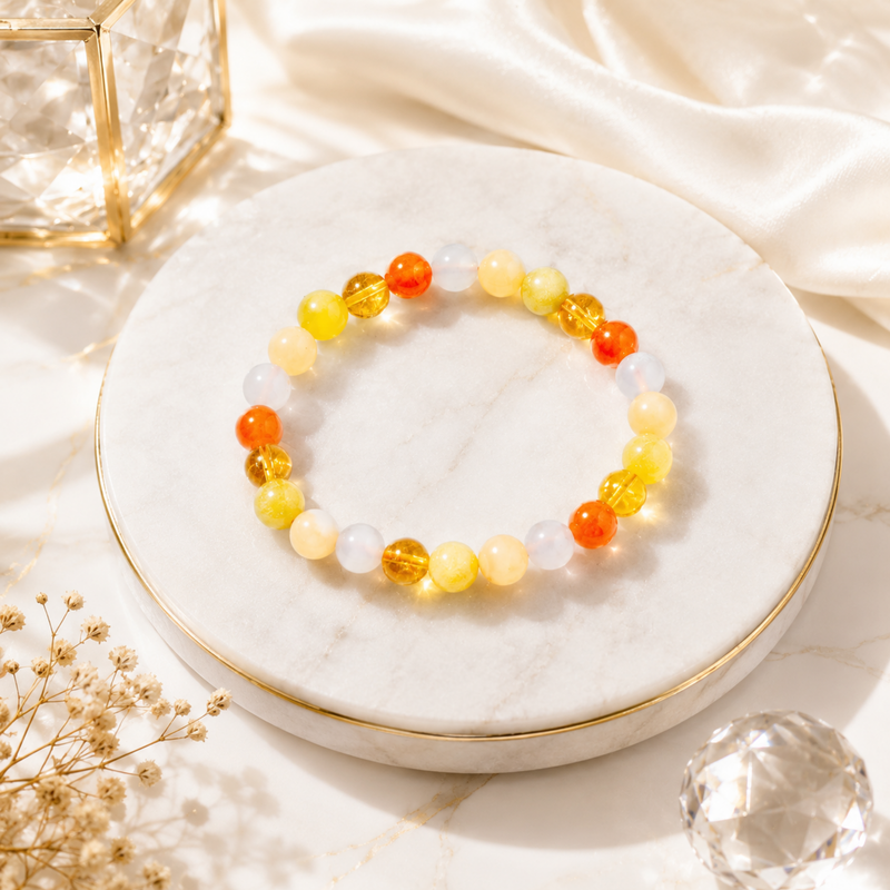 RULING NUMBER 3 BRACELET with orange, yellow, and white translucent beads, displayed on a round white marble tray with gold trim.