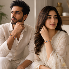 A man and a woman wearing RULING NUMBER 9 BRACELET, posed in a warm, softly lit indoor setting. The man wears a white shirt, and the woman wears a white embroidered top.