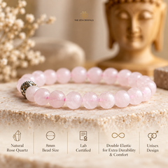 A pink rose quartz beaded bracelet with a silver spacer bead, displayed on a stone slab with a Buddha statue in the background. Text at the bottom lists product features including natural rose quartz, 8mm bead size, lab certified, double elastic, and unisex design.